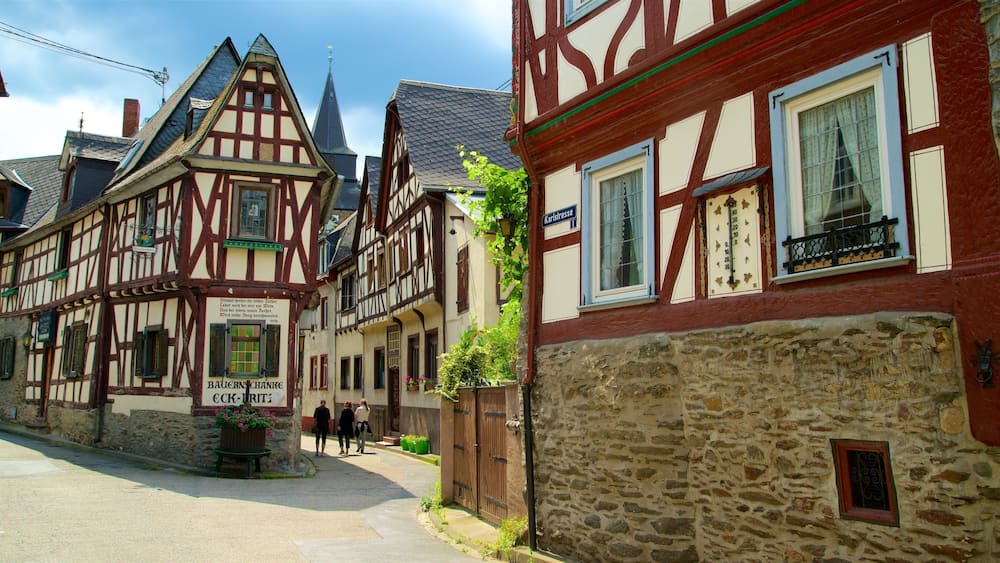 Une rue bordée de maisons traditionnelles à colombages, d’un mur de pierre et d’une enseigne en allemand.