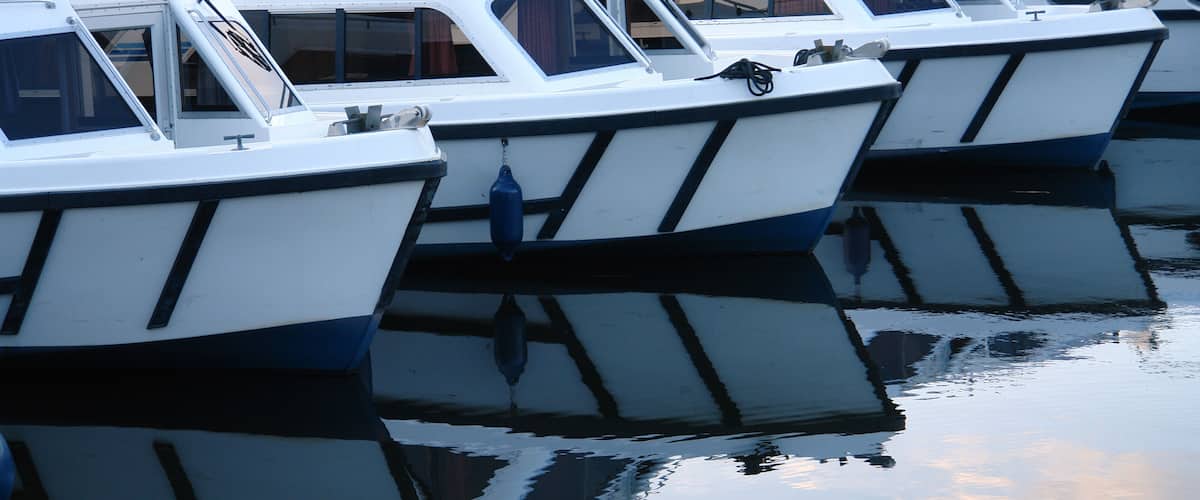 Several white and blue boats docked at a marina with calm water reflecting the boats and sky.