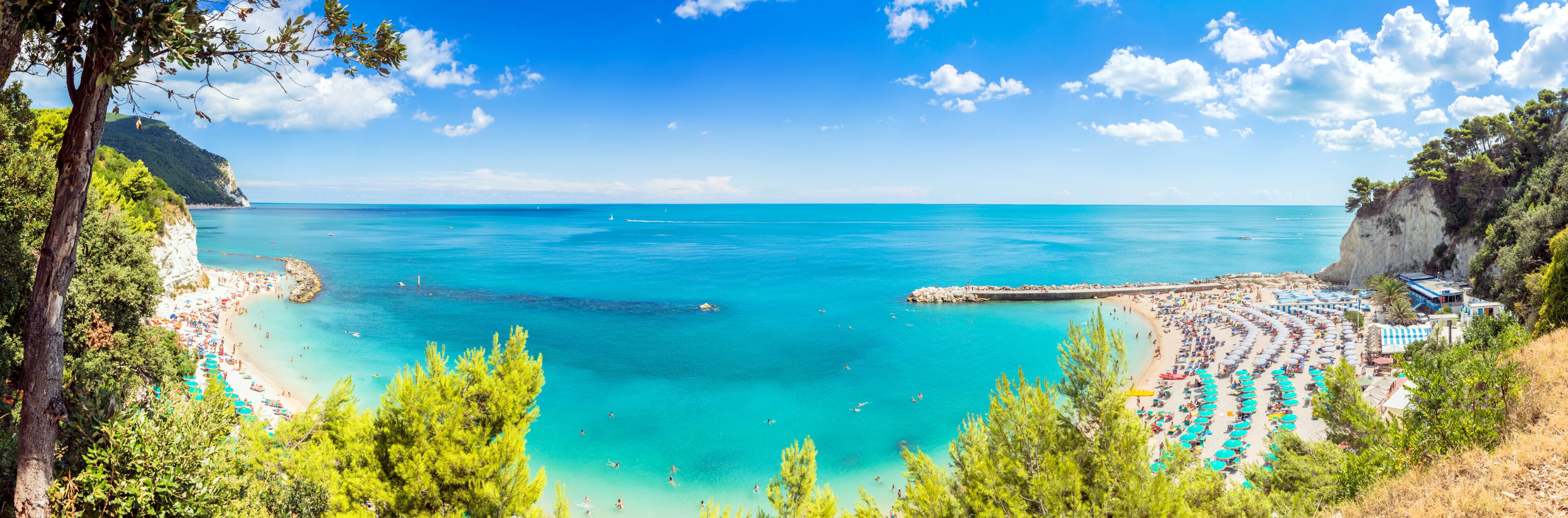 A coastal beach with clear turquoise waters, a rocky coastline, and lush greenery.