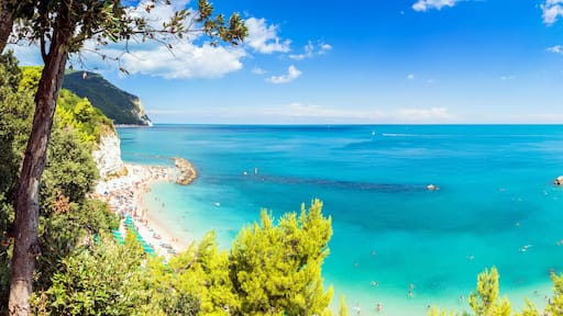 A coastal beach with clear turquoise waters, a rocky coastline, and lush greenery.