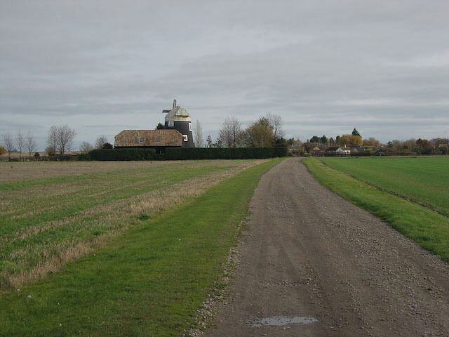 A rural road leading to a farm with a silo and a building.