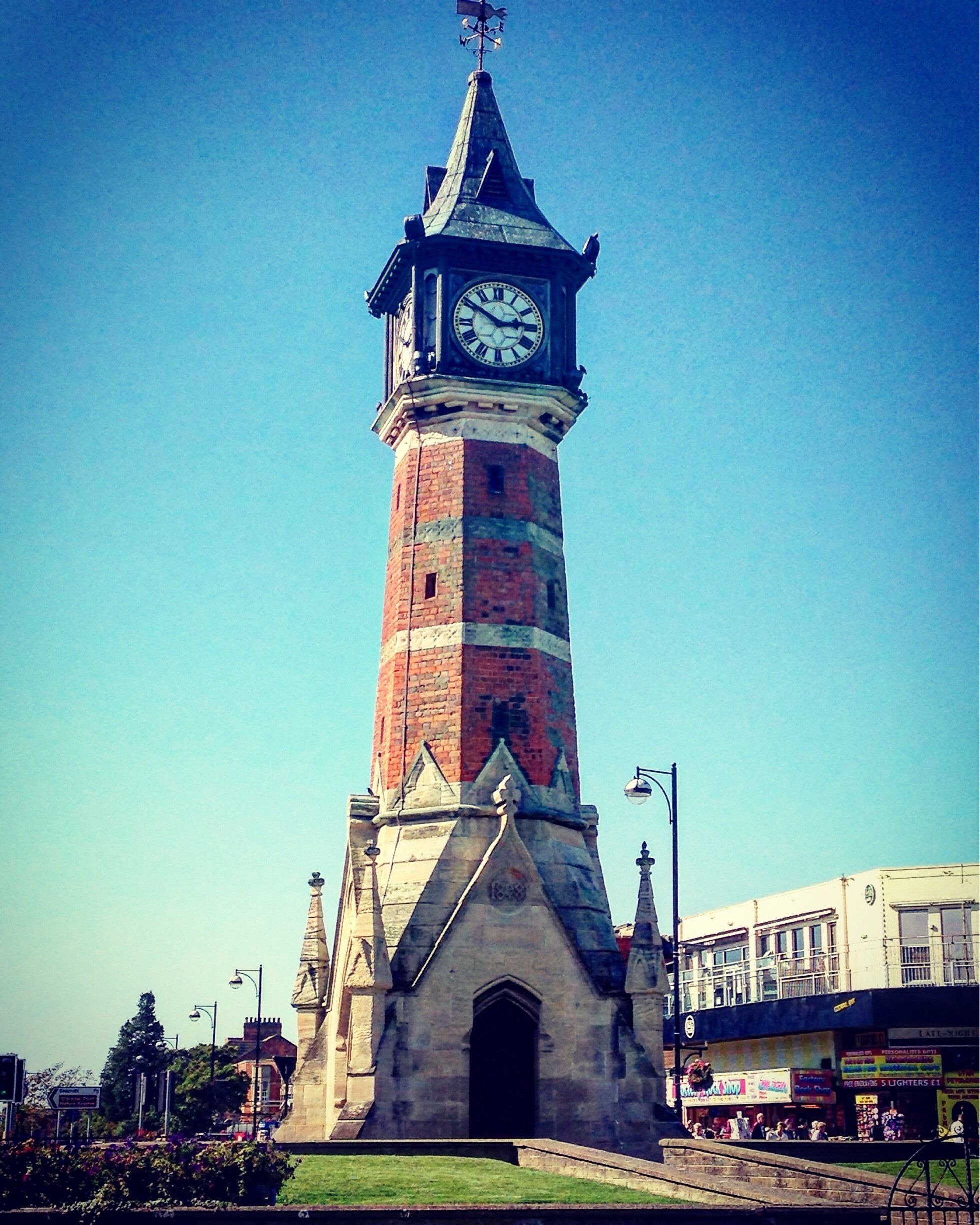 A tall brick clock tower with a weather vane on top.