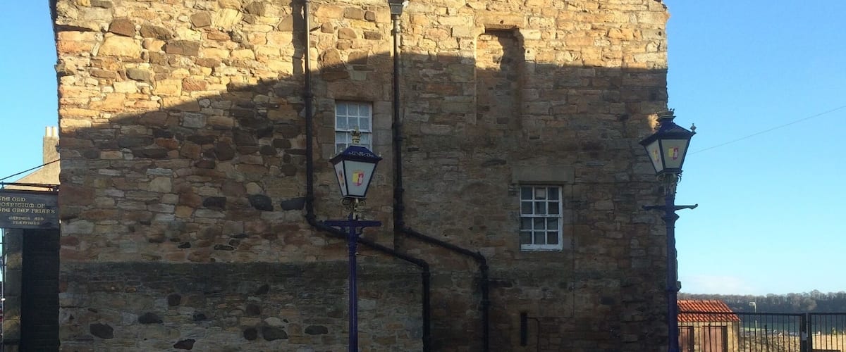 A stone building with a triangular roof and a street lamp in front.