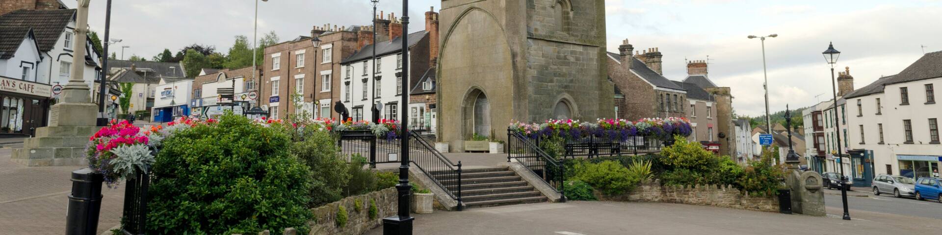 A historic tower with a clock, surrounded by cobblestone streets and flower beds.