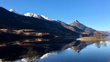 A mountain range with snow-capped peaks and a calm lake reflecting the scenery.
