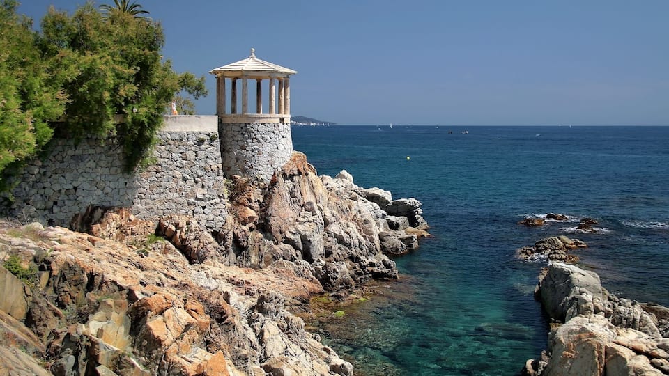 A rocky coastline with a stone tower and clear blue sea.
