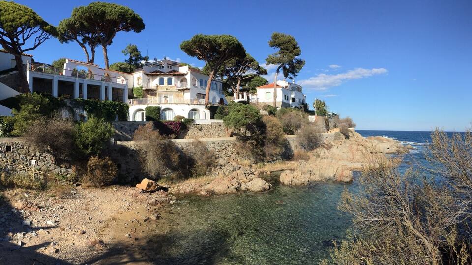 Eine Küstenvilla mit klarem Wasser, felsigem Ufer und dichter umliegender Vegetation.