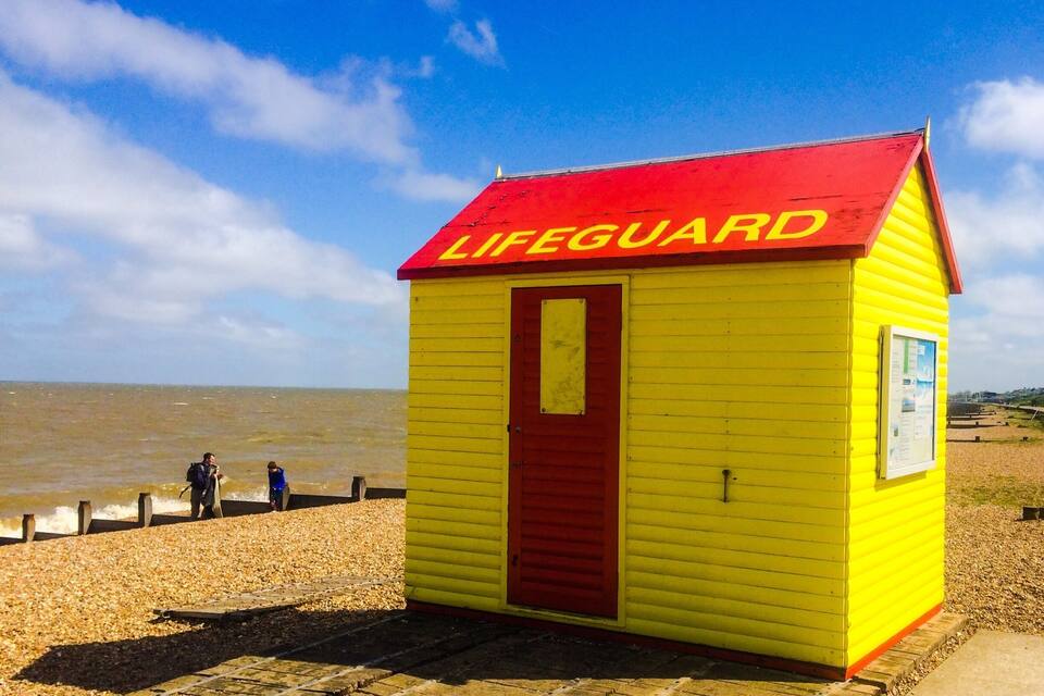 A lifeguard station on a beach with a red roof and yellow walls.