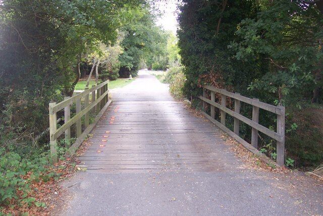 A wooden bridge over a paved path surrounded by trees.
