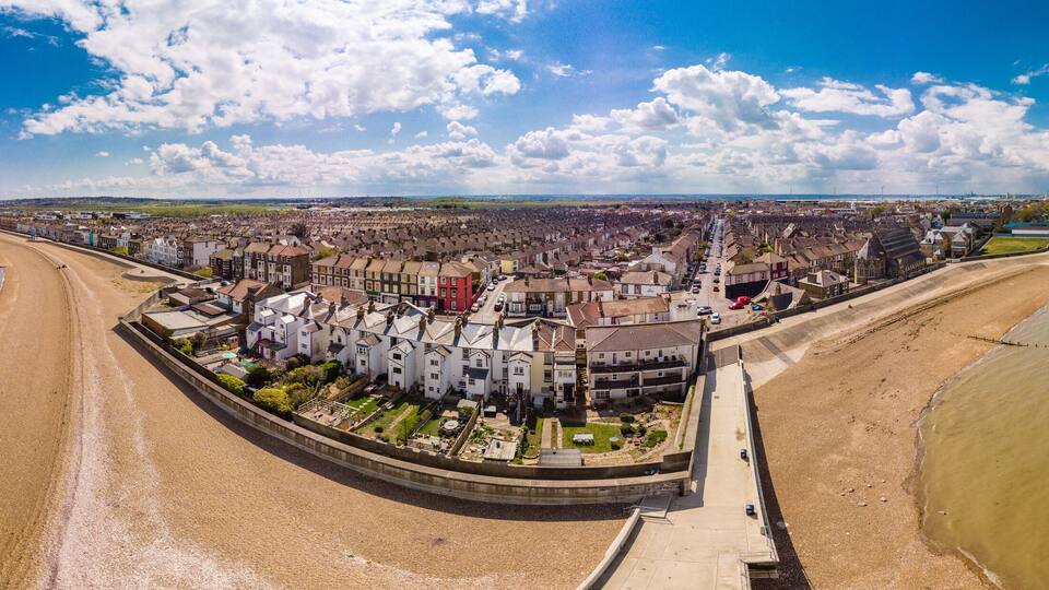 An aerial view of a coastal town with a beach, houses, and a pier.