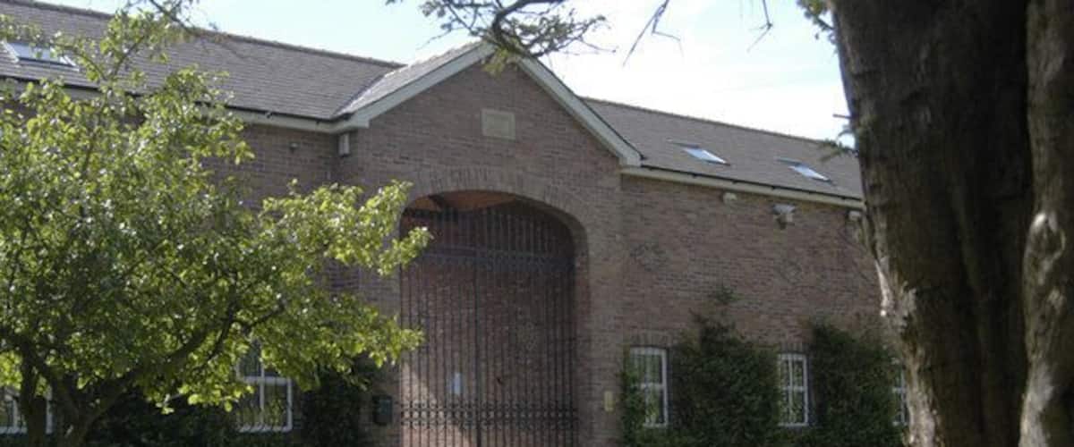 A brick building with a large arched entrance, a tree in the foreground, and a well-maintained lawn.