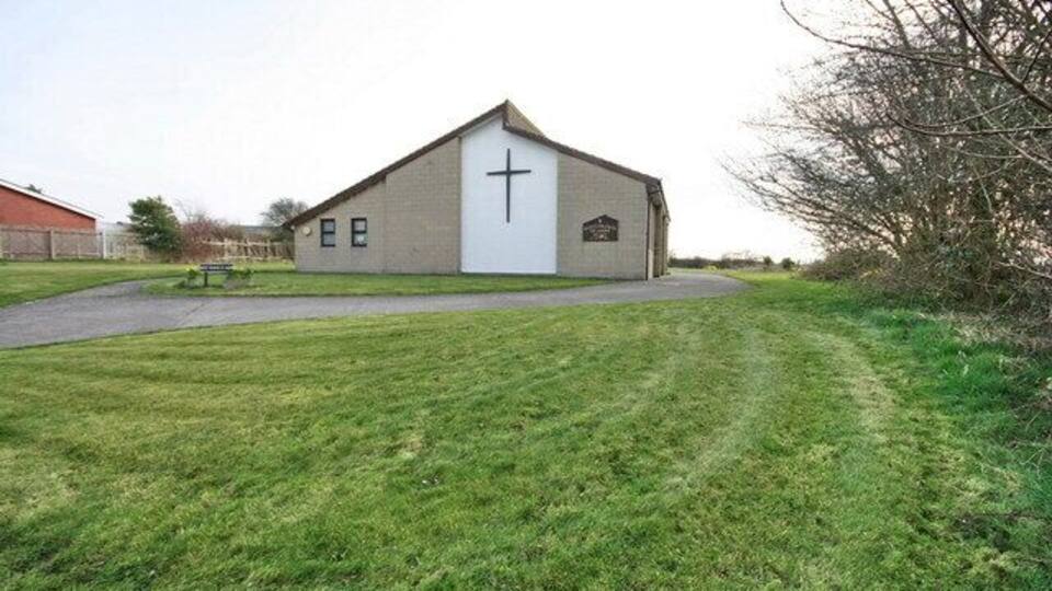 A church with a cross on the front, a paved path leading to it, and a grassy area in the foreground.