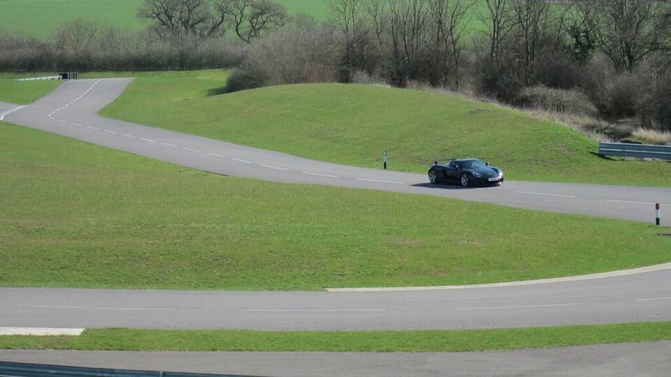A car driving on a winding road through a grassy field with trees in the background.