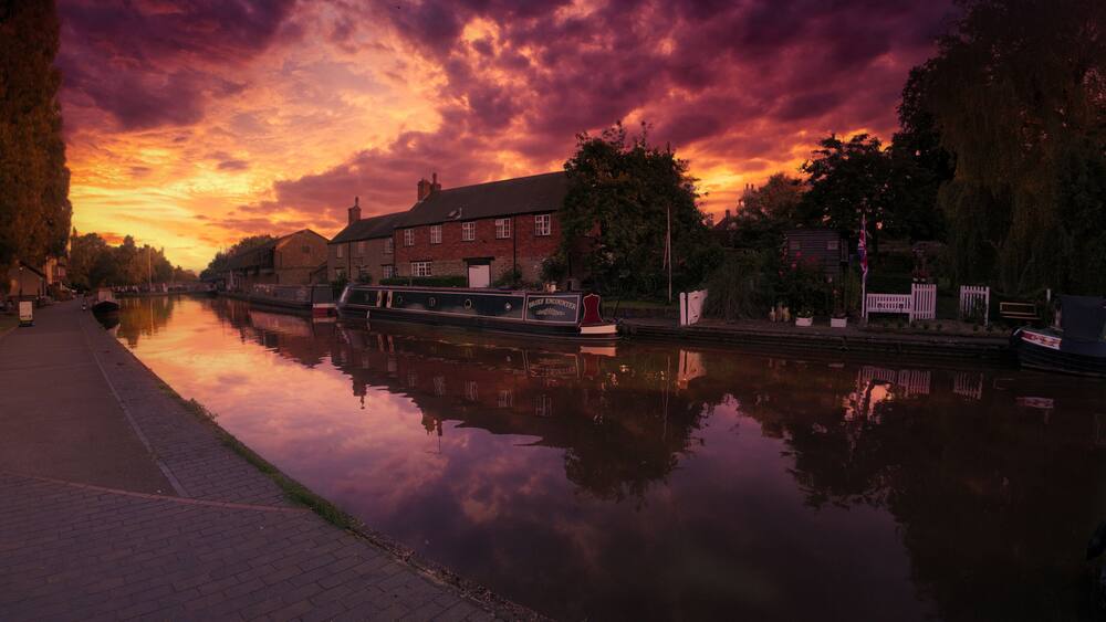 Une rivière paisible reflétant le ciel au coucher du soleil, un canal et une rangée de bâtiments en briques.