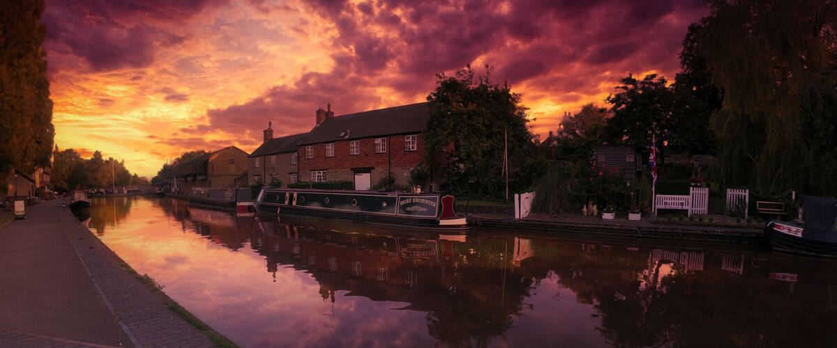 A calm river reflecting a sunset sky, a canal, and a row of brick buildings.