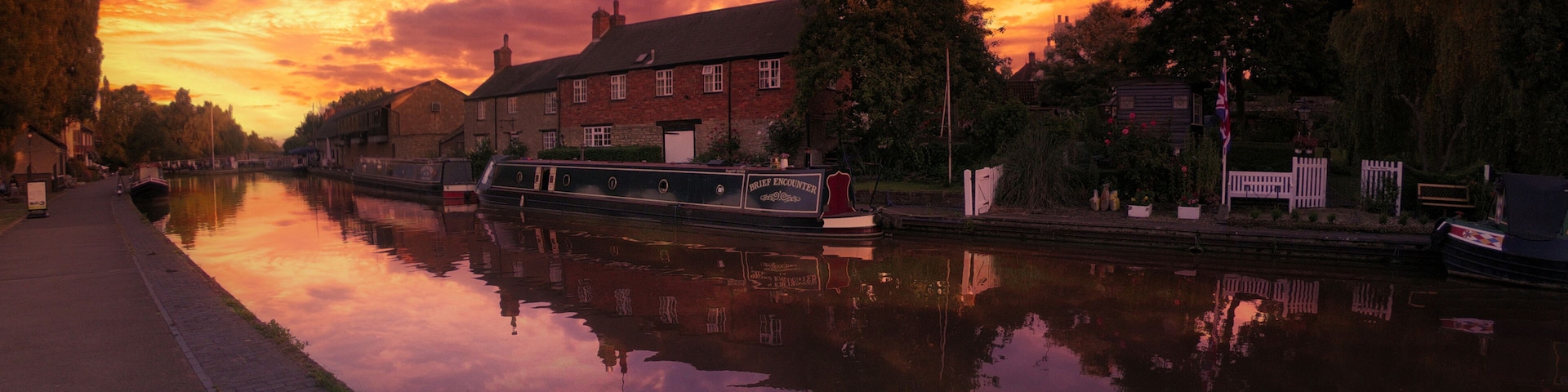 A calm river reflecting a sunset sky, a canal, and a row of brick buildings.