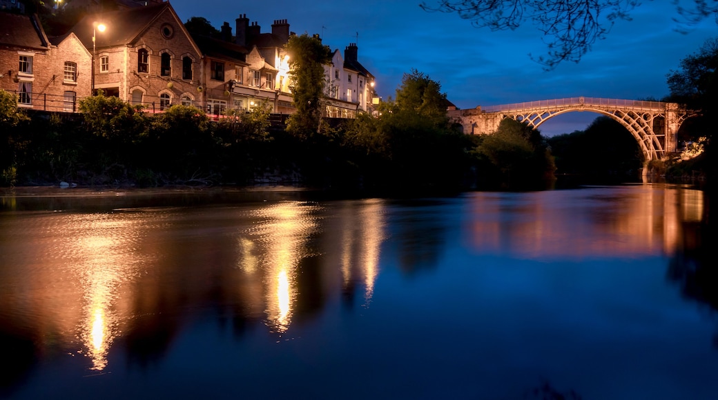 Un río que refleja un puente iluminado y edificios históricos al anochecer.