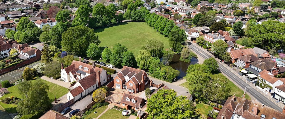 An aerial view of a residential area with houses, a central green field, and surrounding trees.