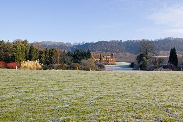 A frosty field with a house and trees in the background.
