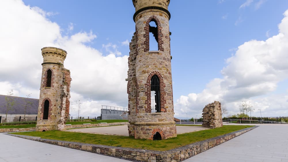 Two stone towers with arched windows and a grassy area in the foreground.