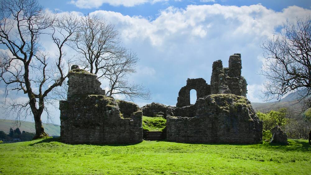 A historic stone ruin with arches and a grassy field.