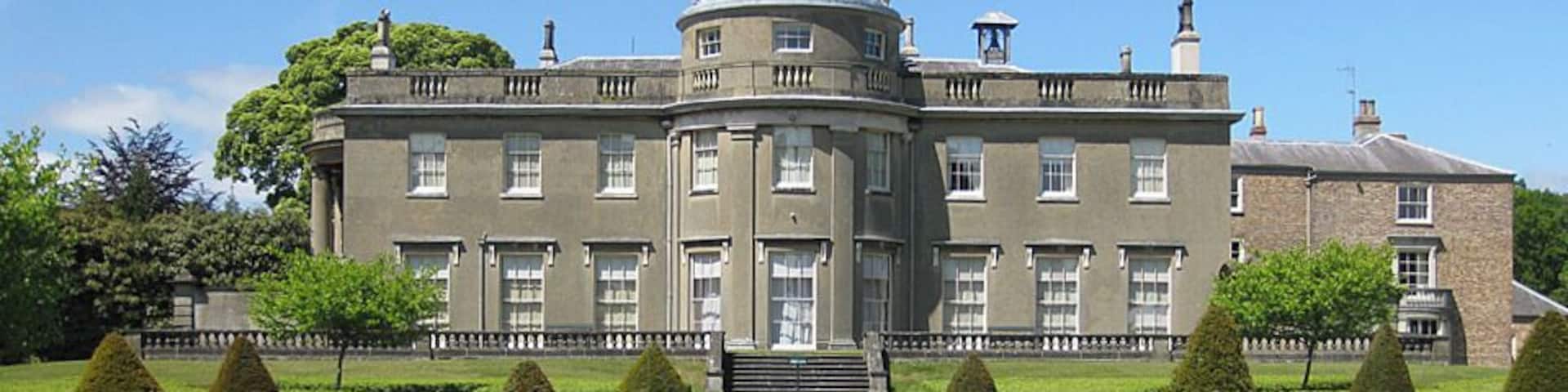 A large stately building with a central dome, surrounded by well-manicured hedges and a formal garden.