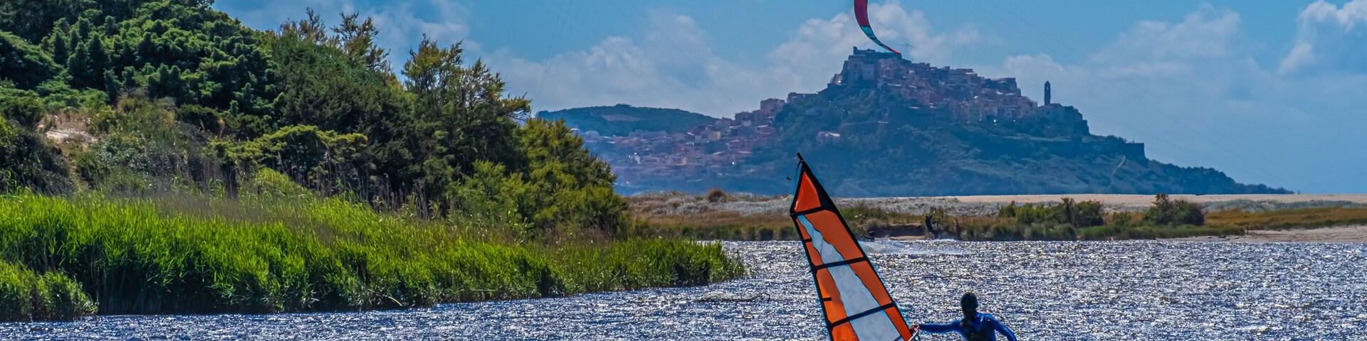 Una persona practica windsurf en una masa de agua tranquila, con varios cometas al fondo.