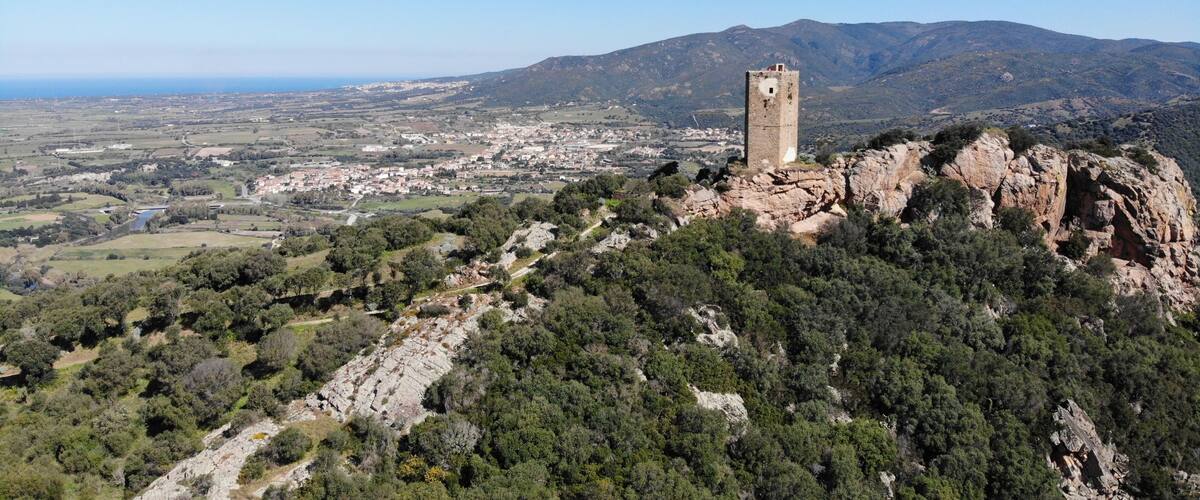 A tower on a hill overlooking a town and mountains.