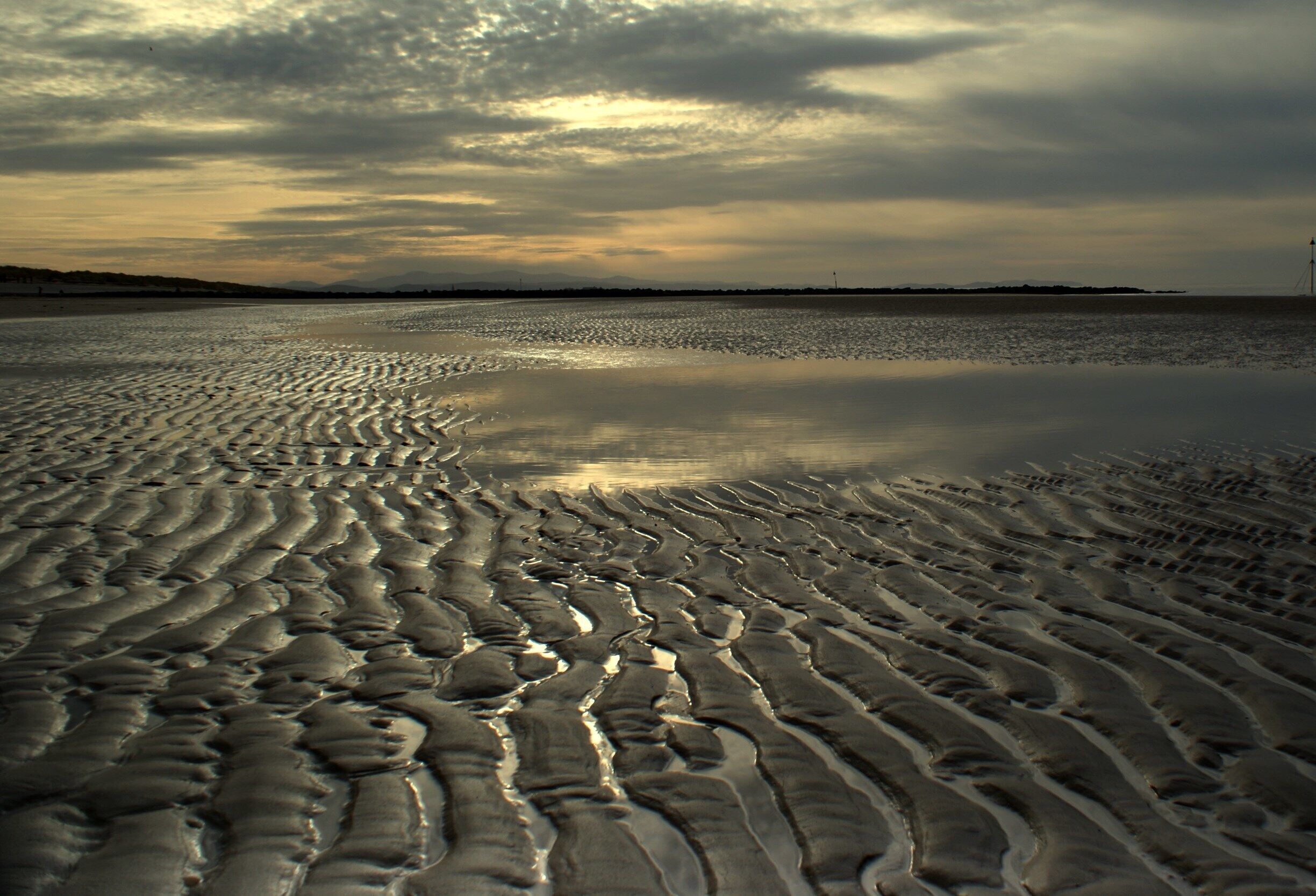 A beach with rippled sand patterns and a cloudy sky.