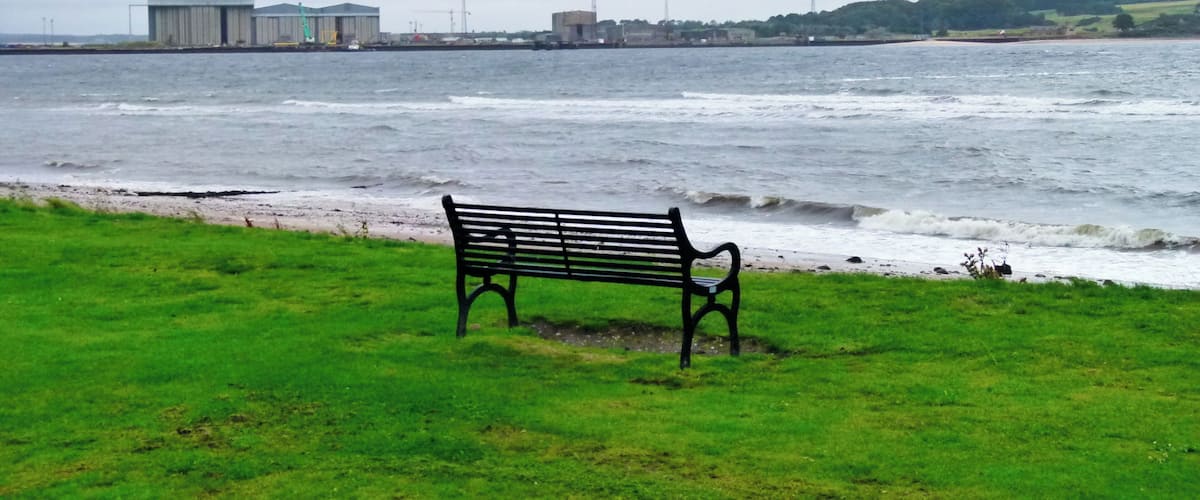 A bench by a beach with waves crashing onto the shore.