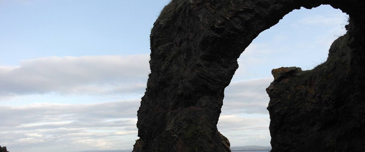 A natural rock arch formation with a view of the sea and distant land.