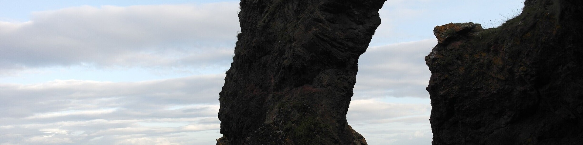 A natural rock arch formation with a view of the sea and distant land.