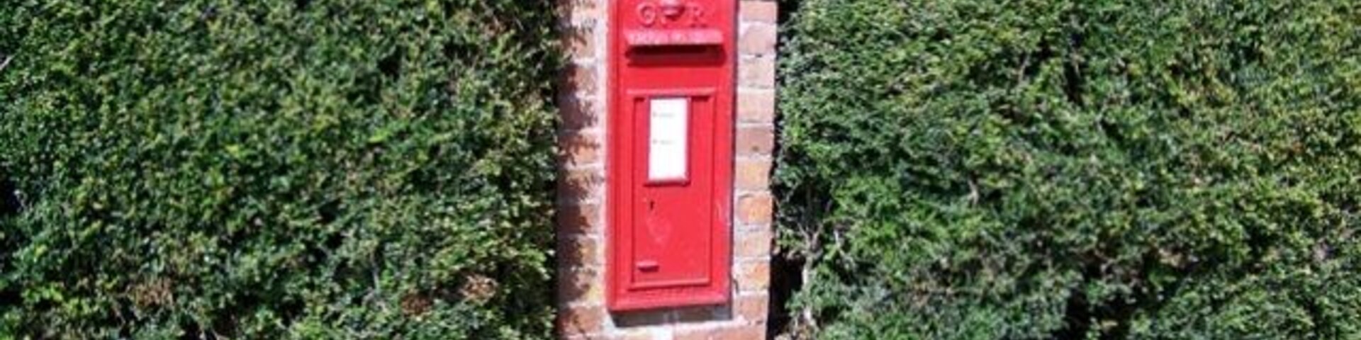 Un buzón rojo en una estructura de ladrillo rodeado de setos verdes frondosos.