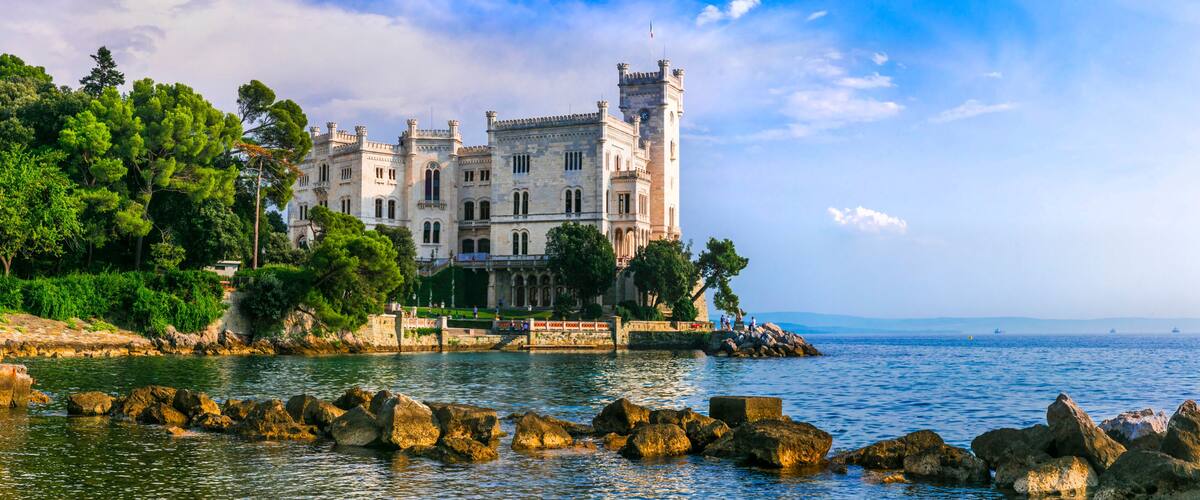 A historic castle by a calm sea with rocky shores and lush greenery.