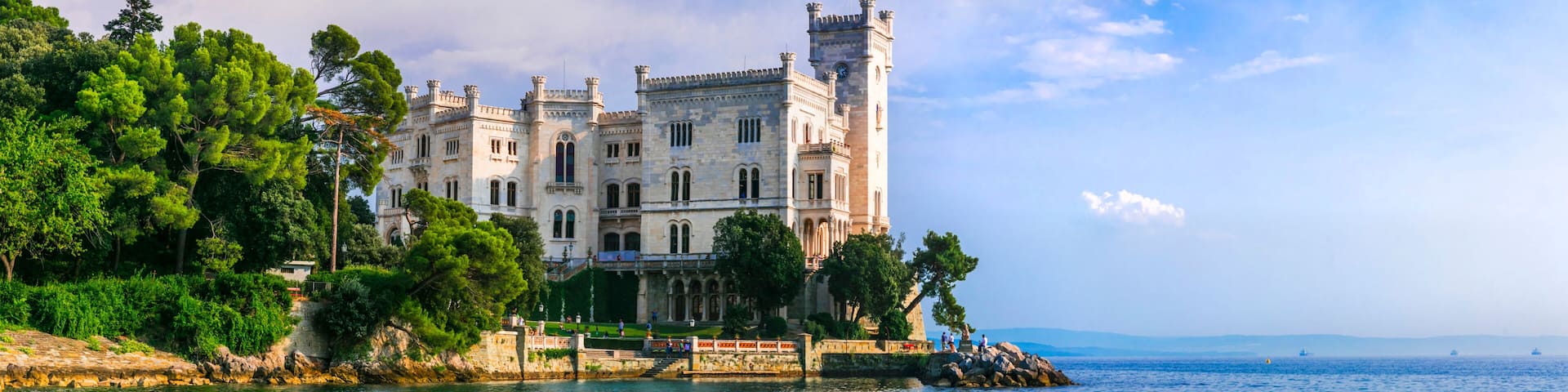 A historic castle by a calm sea with rocky shores and lush greenery.