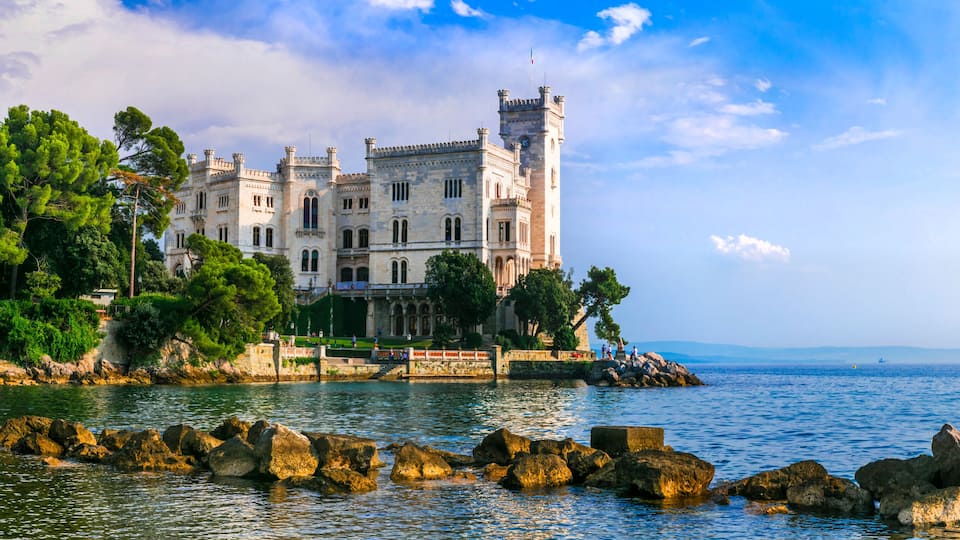 A historic castle by a calm sea with rocky shores and lush greenery.