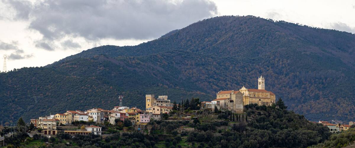 A historic town with a prominent church on a hill, surrounded by lush greenery and a mountain backdrop.
