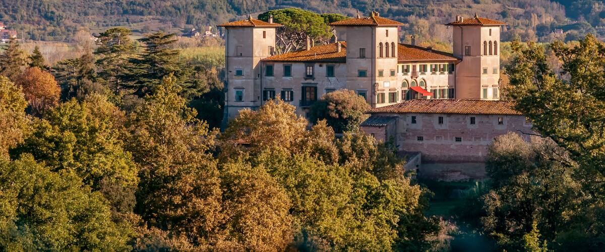 A historic building with a tower, surrounded by trees and hills.