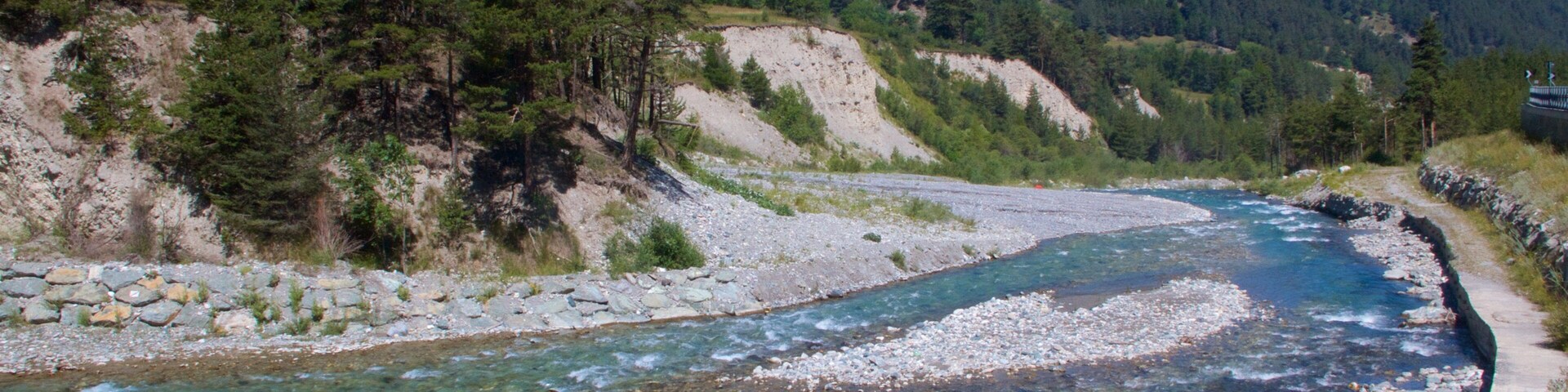 Un río serpentea a través de un paisaje montañoso con orillas rocosas y densos bosques.