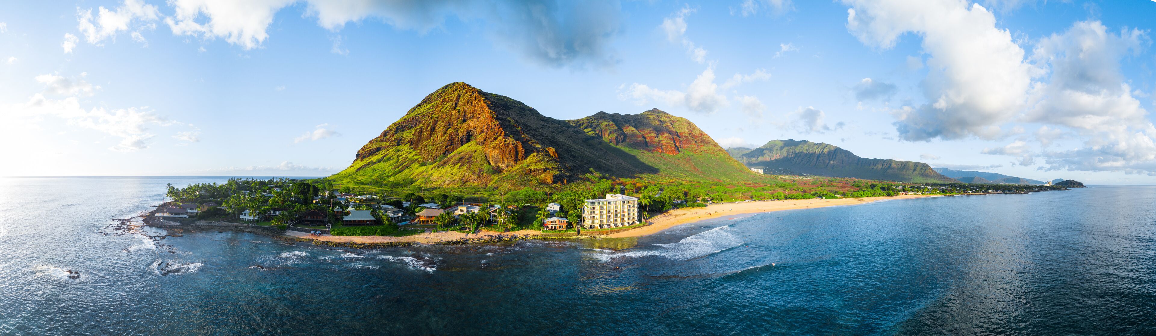 A coastal town with a prominent mountain, clear blue sea, and a sandy beach.