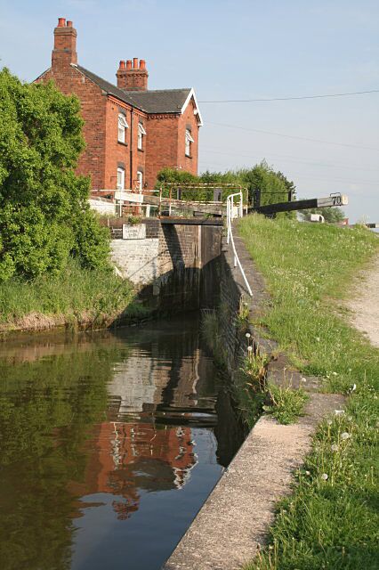 A narrow canal with a lock, a brick building, and a grassy embankment.