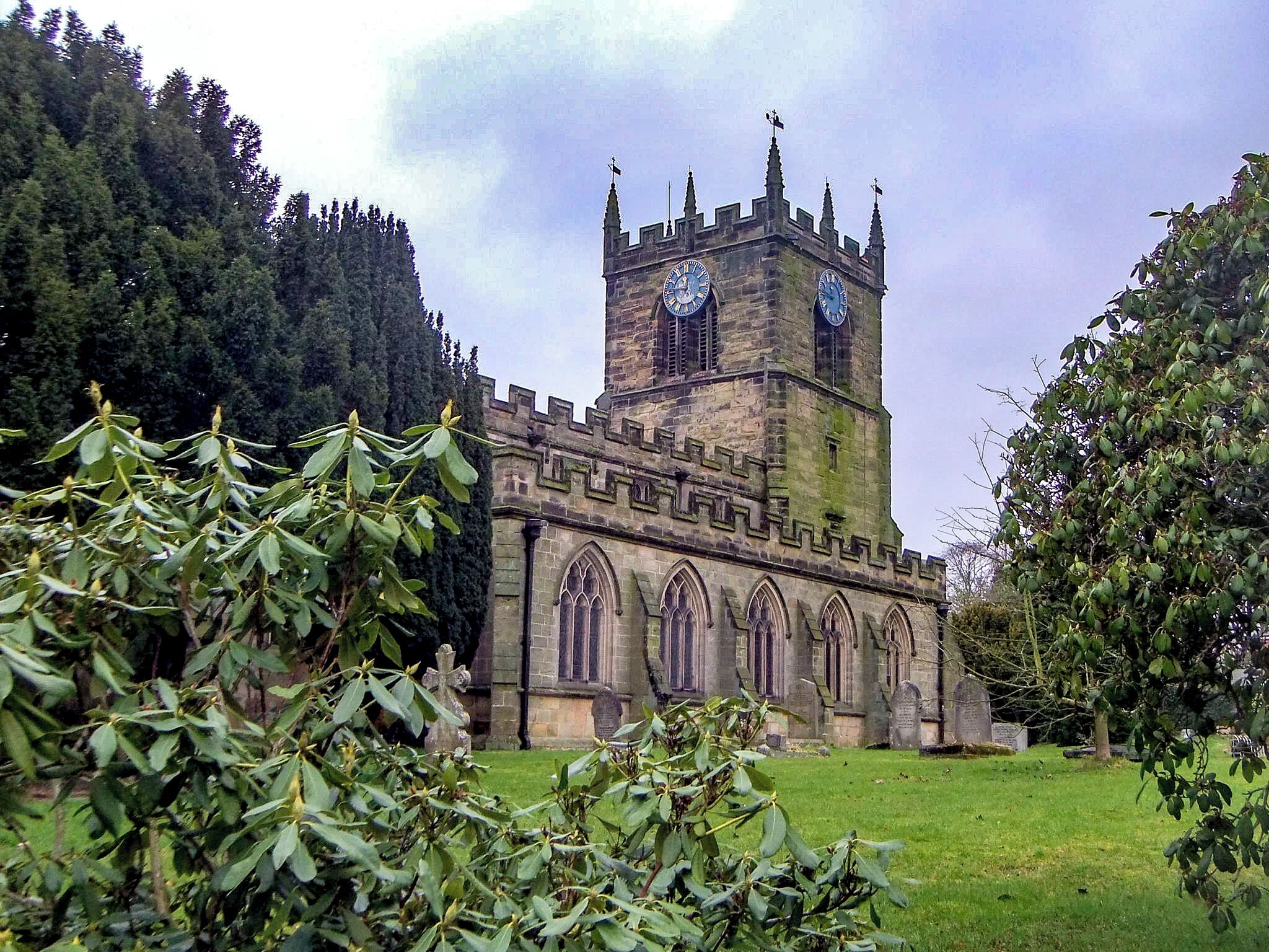 A historic stone tower with a clock, surrounded by a lush green landscape and dense trees.