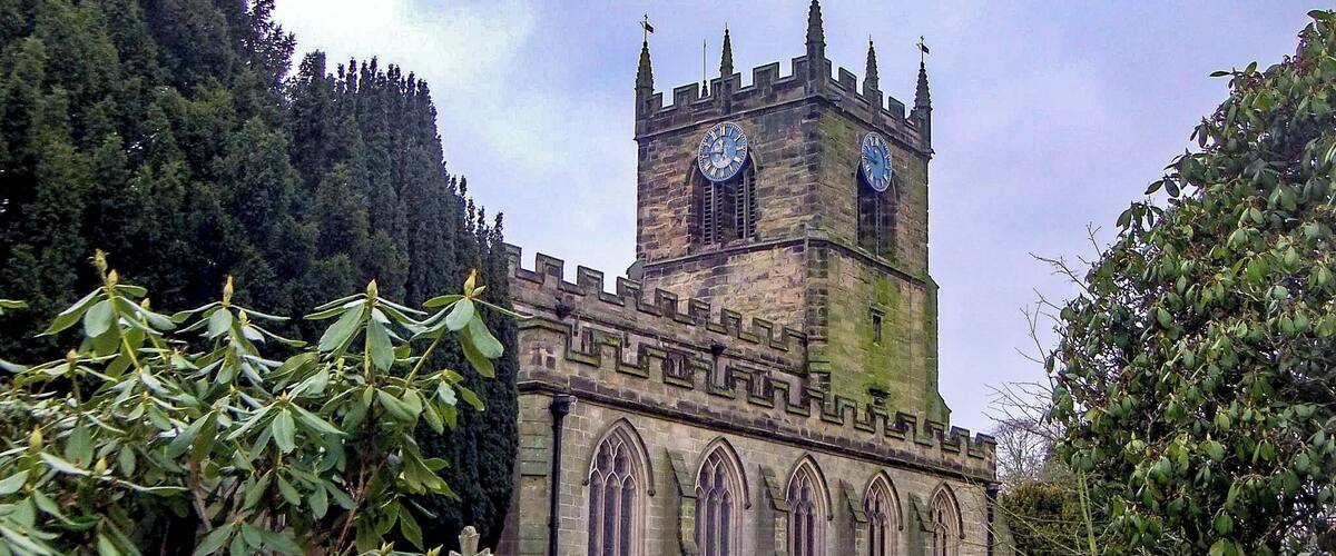 A historic stone tower with a clock, surrounded by a lush green landscape and dense trees.