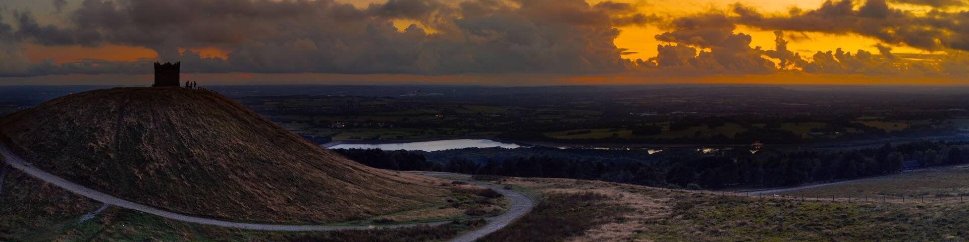 A sunset over a hilly landscape with a path leading to a hilltop structure.