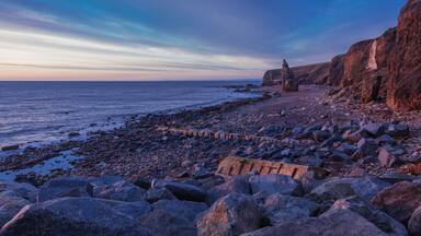 A rocky coastline with large boulders and a cliff.