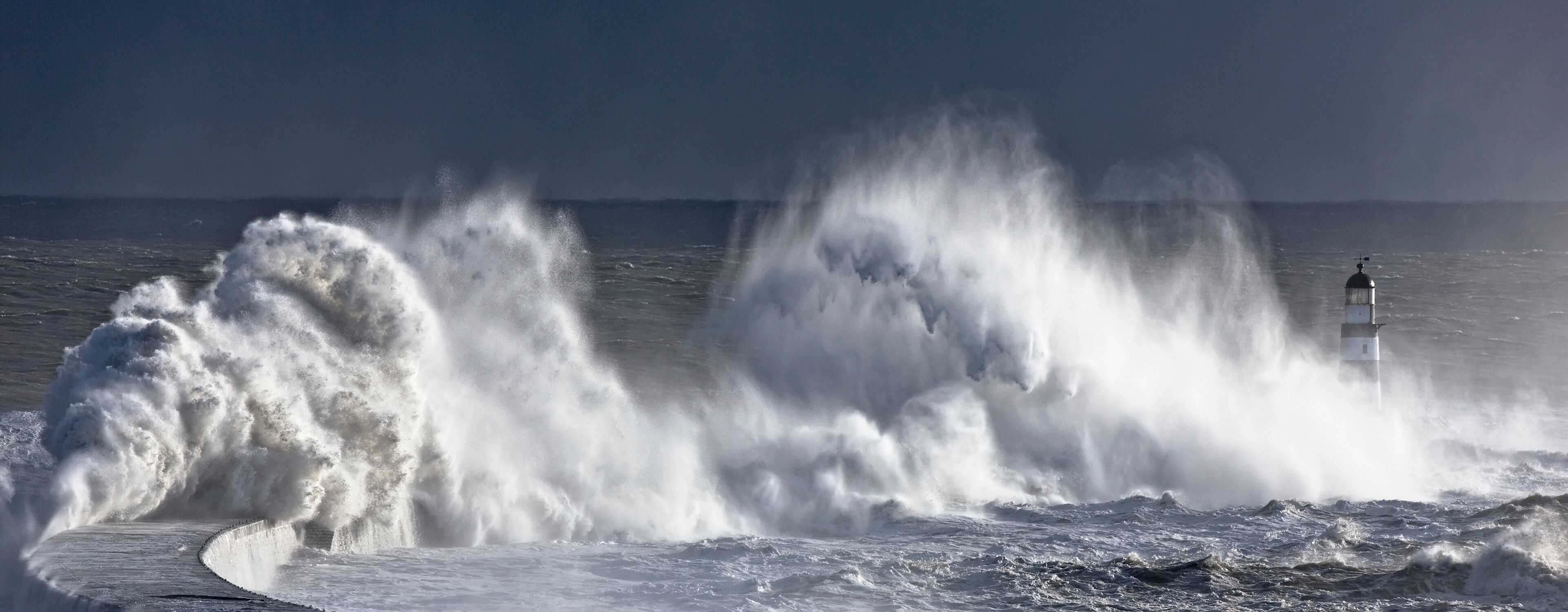 A lighthouse amidst large waves crashing against the shore.