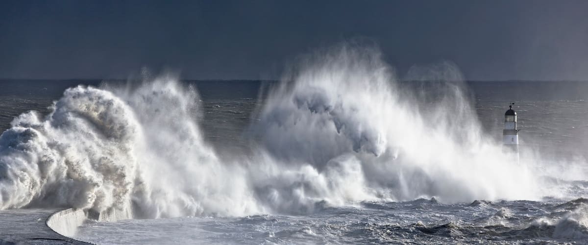 A lighthouse amidst large waves crashing against the shore.