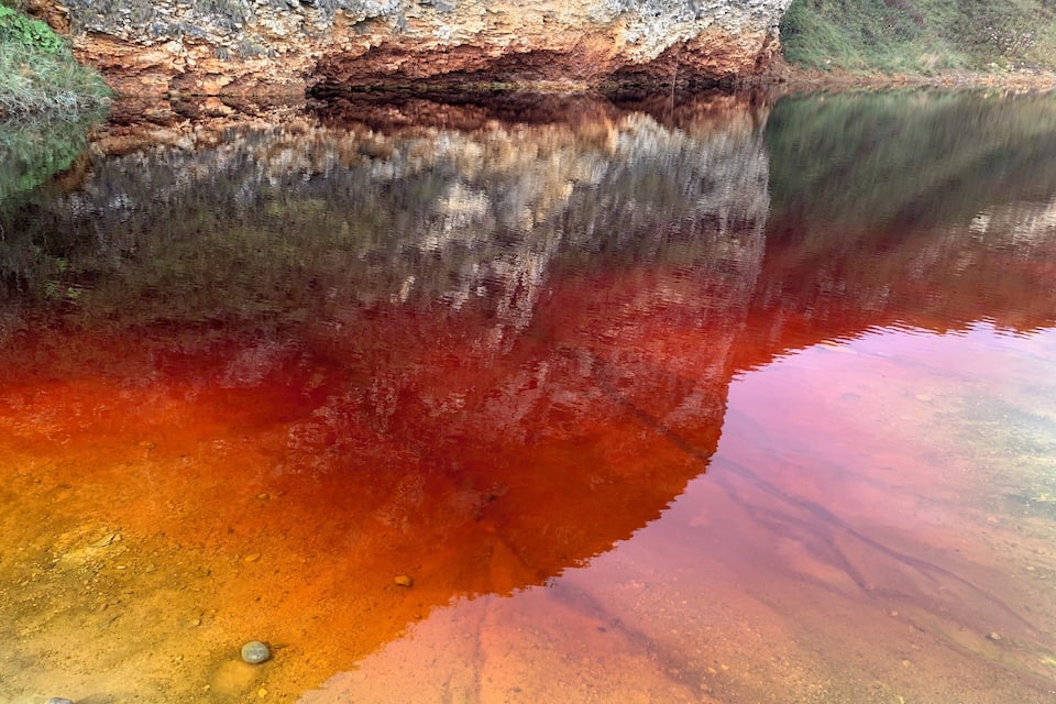 A body of water with a reddish-brown hue, reflecting the surrounding cliffs.