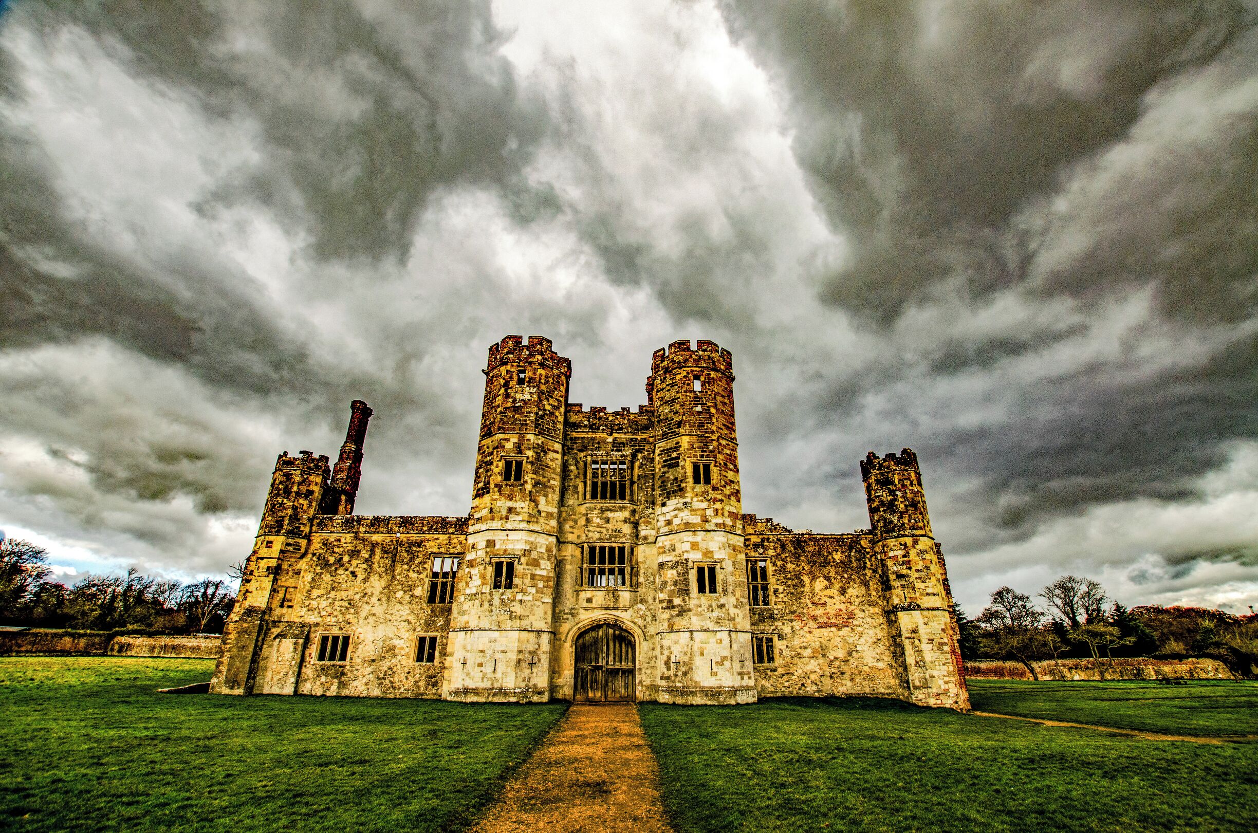 A historic castle with two towers, surrounded by a grassy field and under a cloudy sky.