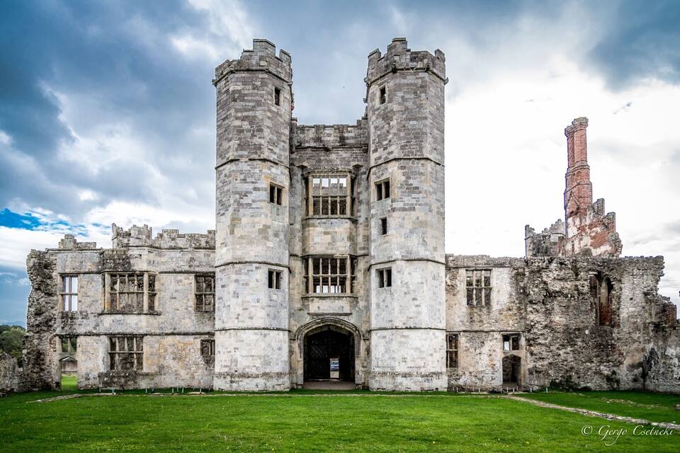 A historic stone castle with two towers, a central archway, and a chimney.